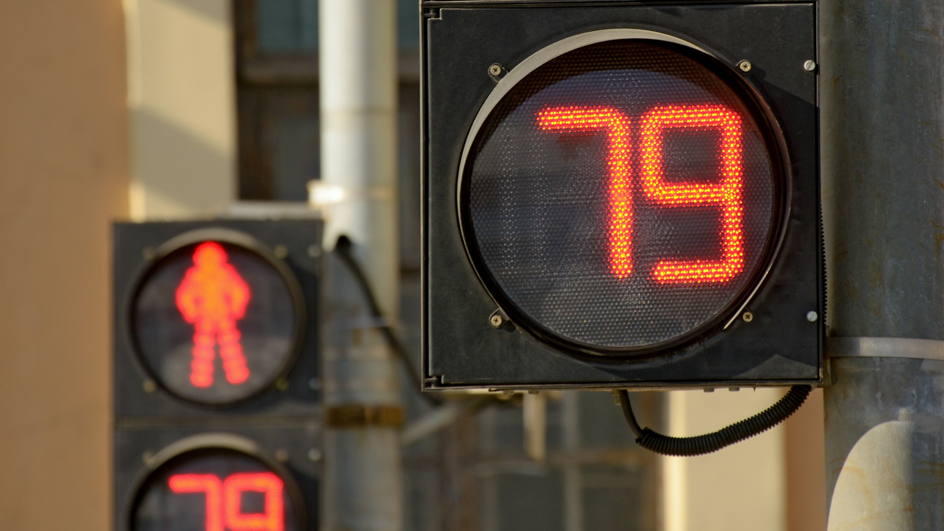  Fotografia aproximada mostra, em primeiro plano, um semáforo fechado para a travessia de pedestres, com o letreiro LED indicando o número "79". Ao fundo, outro semáforo, posicionado à distância, mostra as mesmas informações.